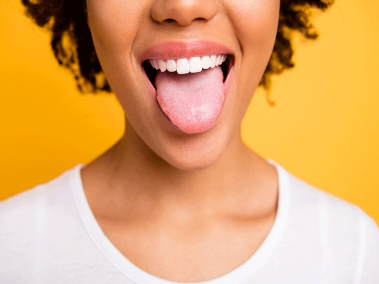 Close-up of a woman's mouth where she is sticking her tongue out flat, showing her white teeth.