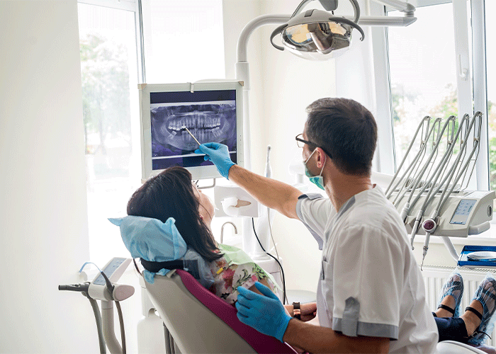 Stock image of a doctor point to an X-ray while having a chair side conversation with a patient.