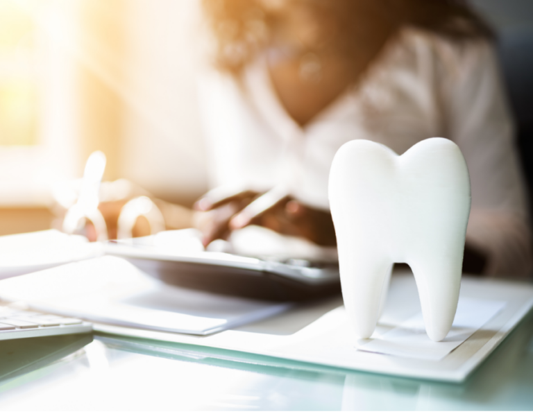 A tooth display on top of the tables together with some papers and calculator. The background is a woman wearing a white top, the setting is office.